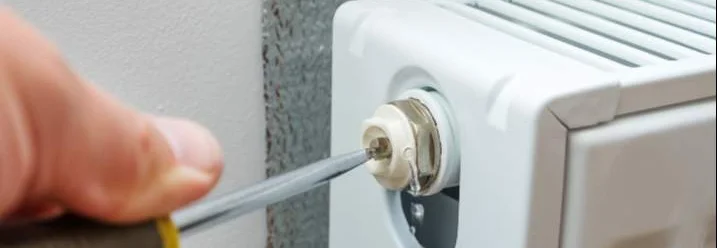 Person entlüftet Heizkörper mit Schraubendreher